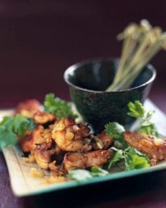 Port-paprika chicken bites garnished with cilantro, piled on a square white plate with a dish of picks.