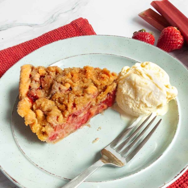 A slice of strawberry rhubarb pie on a green plate with a scoop of ice cream and a fork on the side.