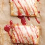 Two homemade toaster tarts on a sheet of parchment drizzled with glaze.