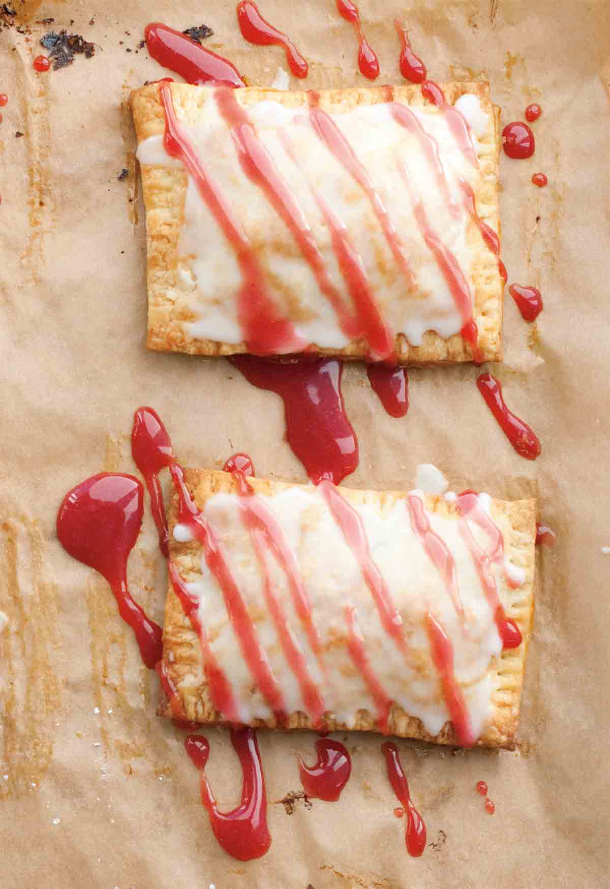 Two homemade toaster tarts on a sheet of parchment drizzled with glaze.
