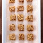 A white baking dish with a piece of patterned parchment and 15 squares of coconut blondies.