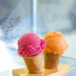Two sugar cones, one filled with a scoop of cantaloupe sorbet, the other with a scoop of hibiscus beet sorbet.