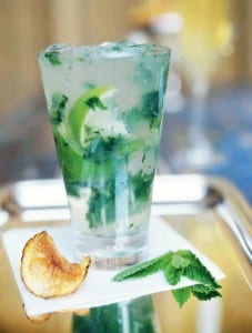 A southside cocktail on a napkin on a silver tray with a potato chip and sprig of mint beside it.