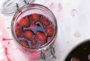 A canning jar filled with cherry liqueur and whole cherries, with a pot of liqueur and many cherry stones beside it.