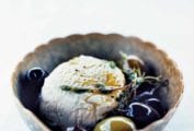 A decorative bowl filled with a sphere of goat cheese and a few olives, topped with a thyme sprig.