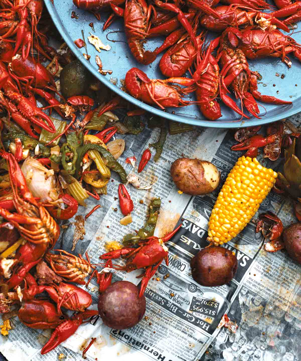 A newspaper-topped table strewn with crawfish, corn, peppers, and potatoes - a classic crawfish boil.