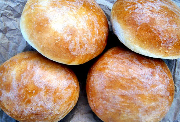 Four homemade burger buns dusted with flour on grey paper.