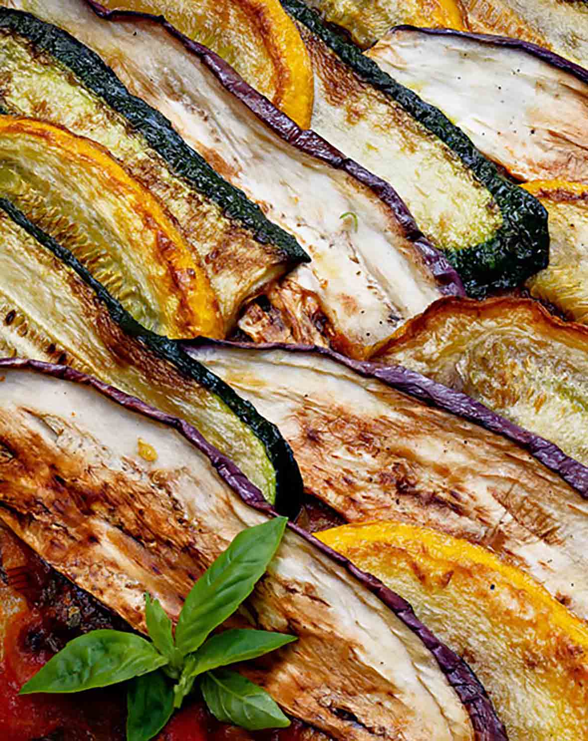 Layers of zucchini, summer squash, and eggplant cooked together and garnished with basil for this summer vegetable gratin.