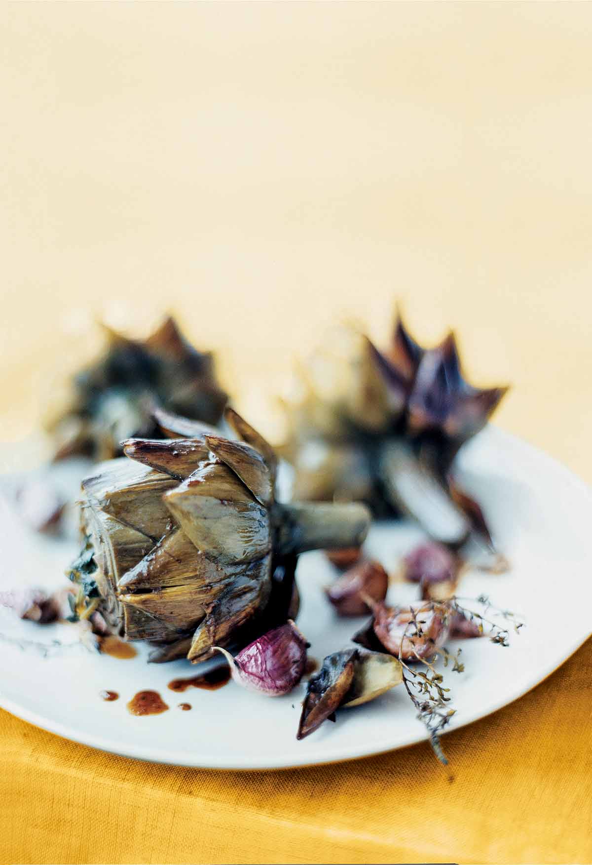 Three braised artichokes with garlic and thyme on a white plate.