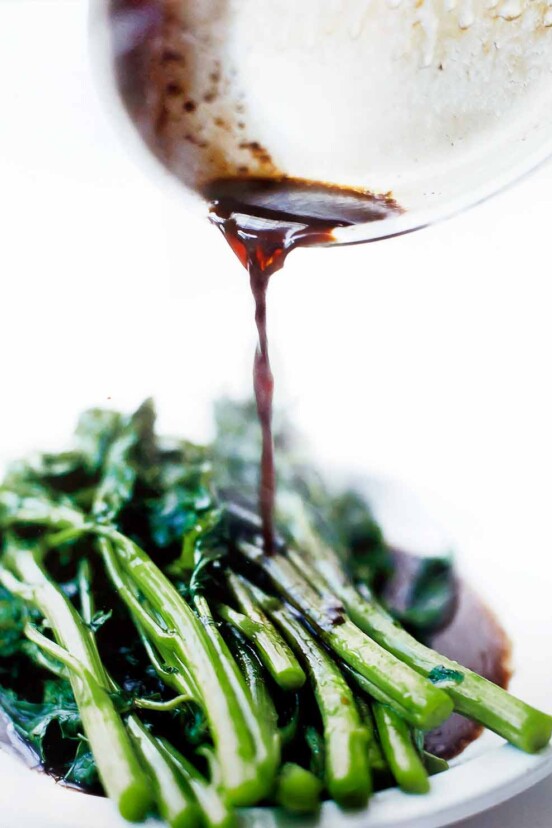A white plate of broccoli rabe with balsamic brown butter being poured on top