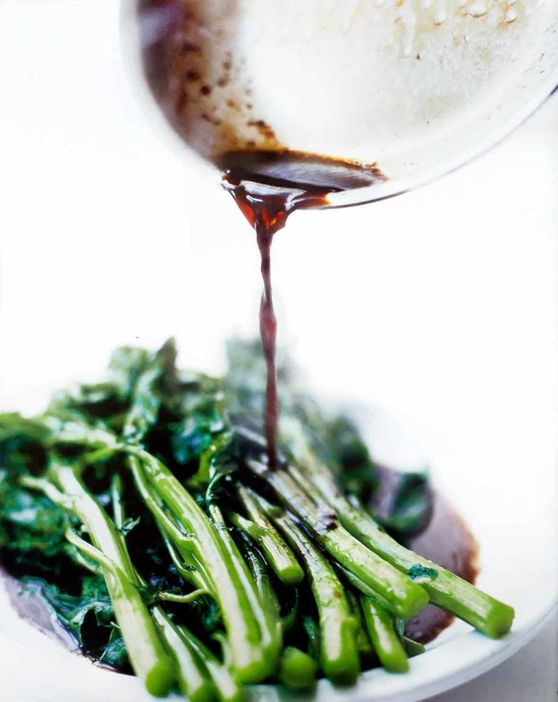 A white plate of broccoli rabe with balsamic brown butter being poured on top