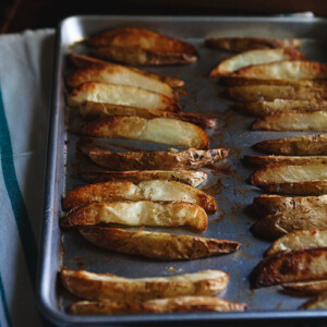 A baking sheet full of oven-roasted fries cut in wedges.