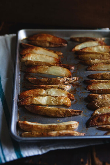 A baking sheet full of oven-roasted fries cut in wedges.
