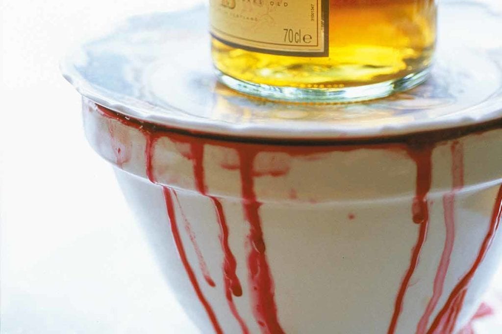 Vindränkt höstpudding i vit skål med vin som droppar ner på sidan toppad med en vit tallrik och en flaska whisky.