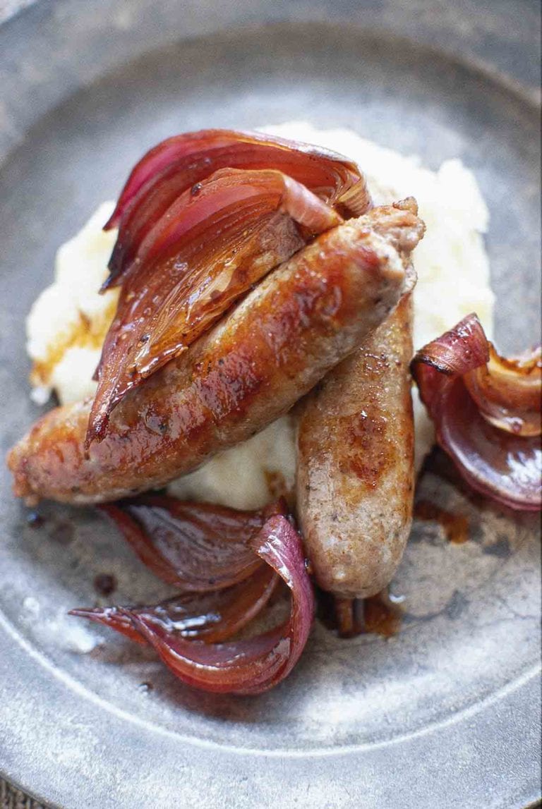 Two bangers and mash with cooked red onion in a bowl.
