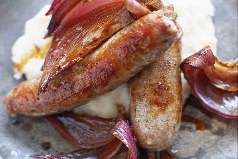 Two bangers and mash with cooked red onion in a bowl.