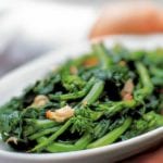 A white platter filled with broccoli rabe, topped with roasted garlic and red pepper flakes.