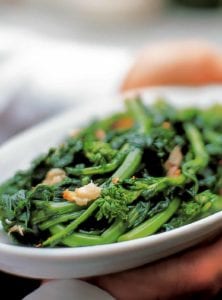 A white platter filled with broccoli rabe, topped with roasted garlic and red pepper flakes.