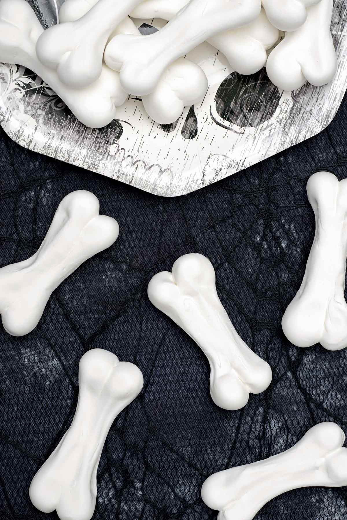 تتراكم عظام الميرانغ في عيد الهالوين على طبق ورقي وتتناثر على مفرش أسود من نسيج العنكبوت بجانب الطبق.