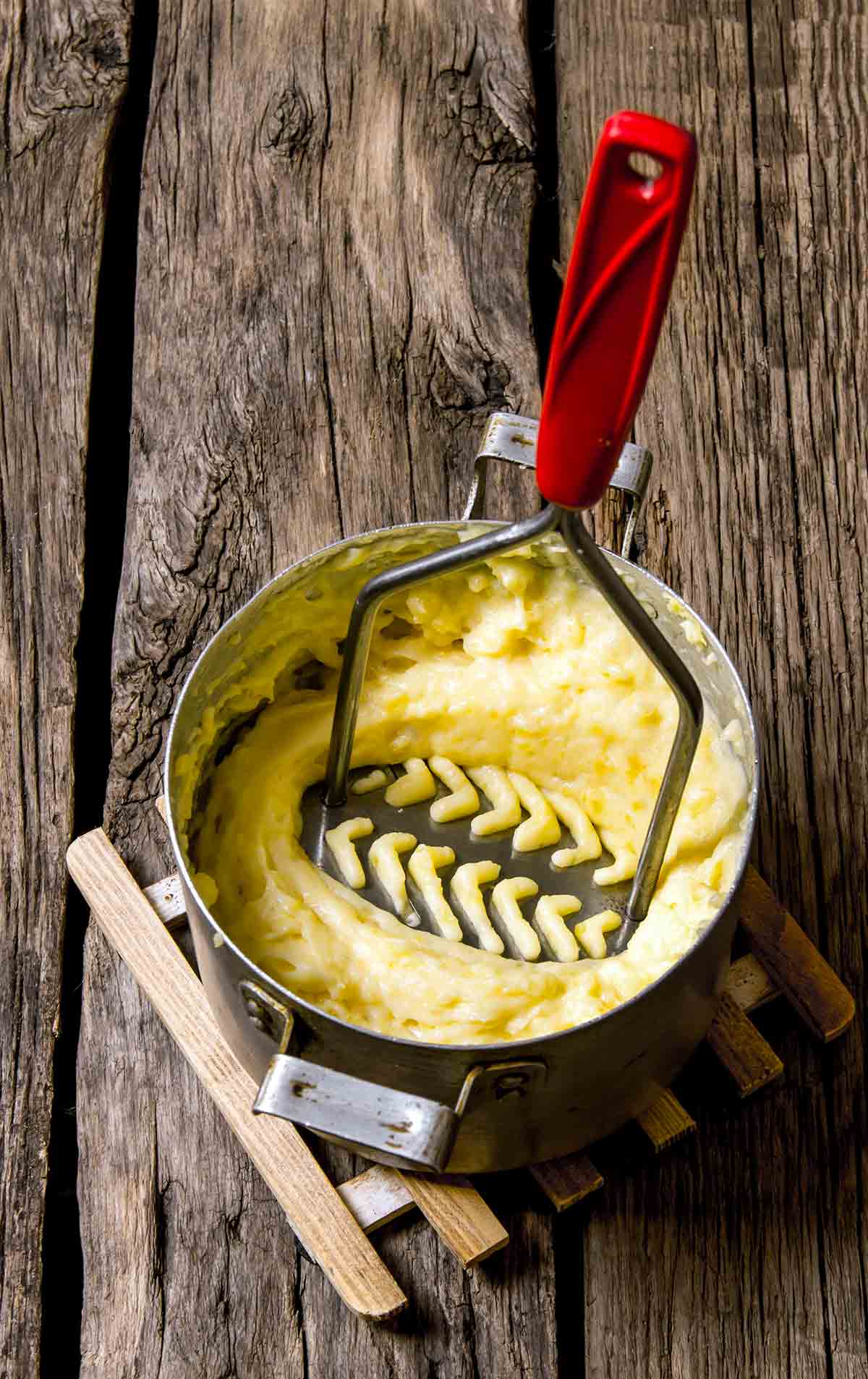 A potato masher pressing down in a pot of olive oil mashed potatoes.