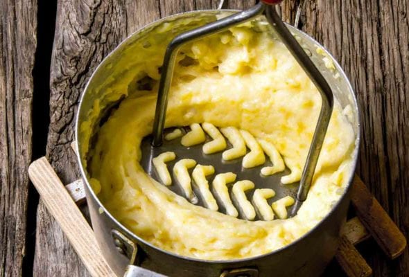A potato masher pressing down in a pot of olive oil mashed potatoes.