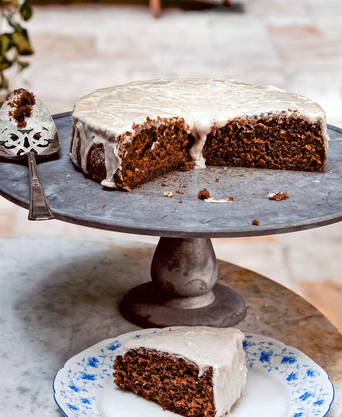 A cut root beer cake on a pewter platter with a slice on a decorative plate in front.