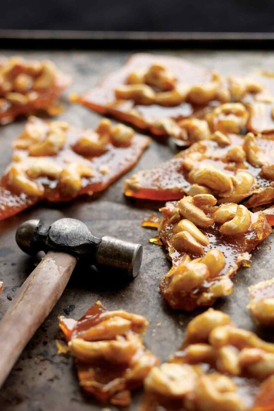 Pieces of broken cashew brittle with a hammer lying beside them.
