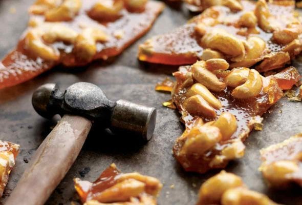 Pieces of broken cashew brittle with a hammer lying beside them.