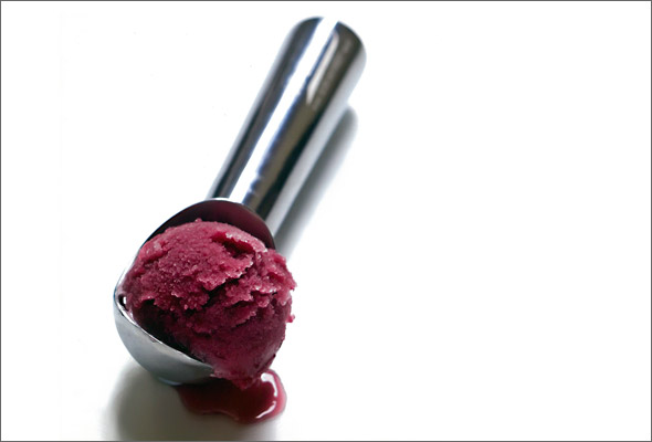A metal ice cream scoop with a scoop of concord grape granita in it.