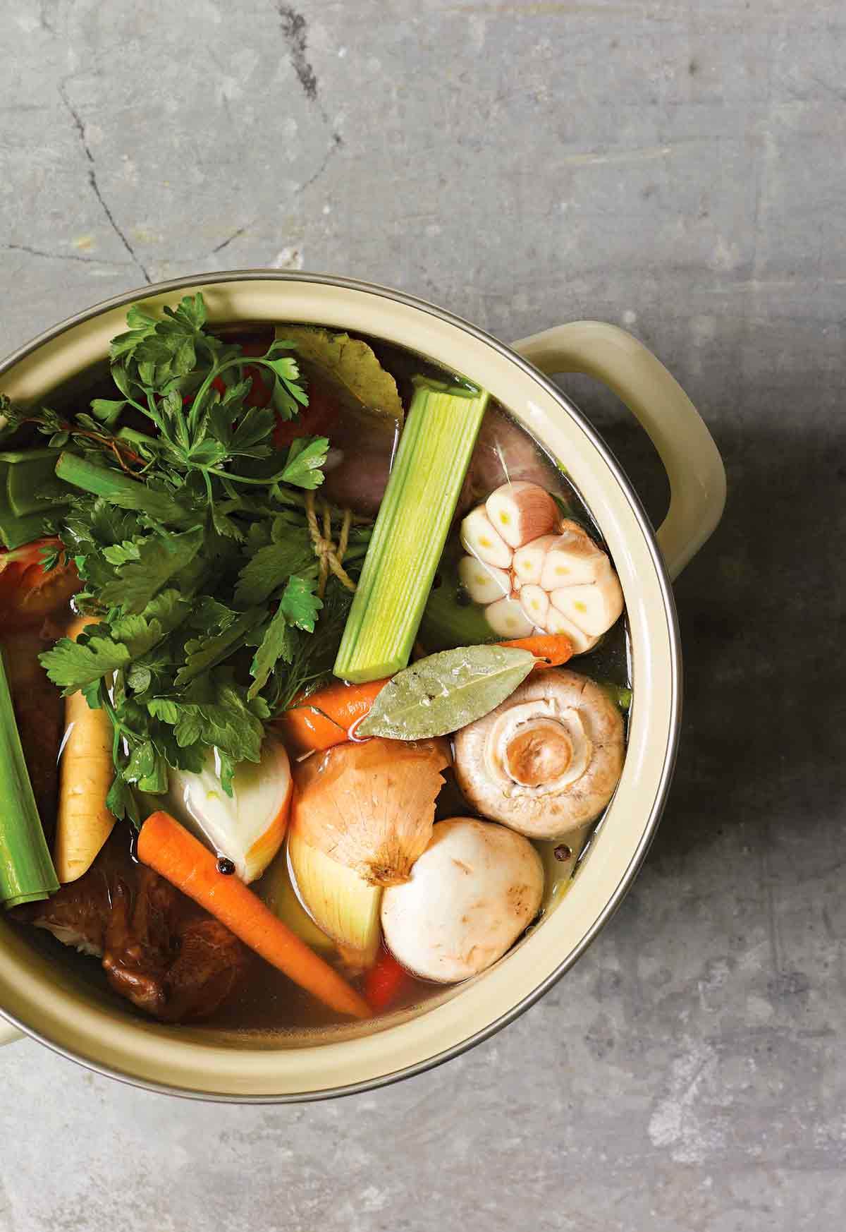 A stock pot filled with mushrooms, leeks, garlic, onion, carrots, and parsley for making roast chicken stock.