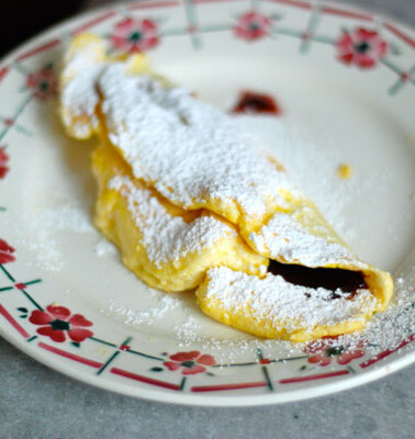 Omelette Confiture photographed on a white plate with flowers and a dusting of powdered sugar on the omelette itself.