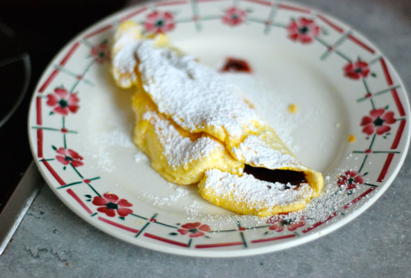 Omelette Confiture photographed on a white plate with flowers and a dusting of powdered sugar on the omelette itself.