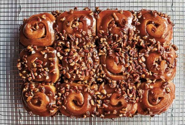 12 schnecken, pecan cinnamon buns, covered with pecan-caramel topping, and chopped pecans on a wire rack