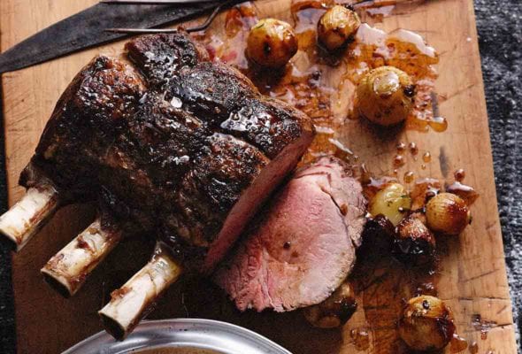 A standing rib roast on a cutting board with caramelized onions