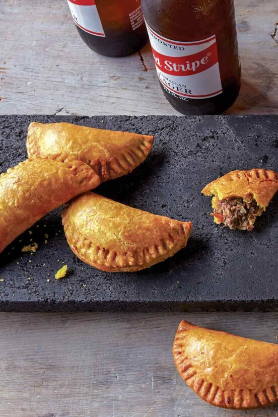 Five half-moon pastries, Jamaican beef turnovers, on a stone plate, three bottles of beer