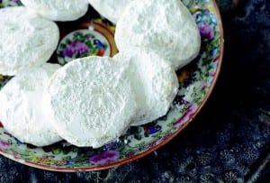 Lemon meltaway cookies, covered in icing sugar, piled on a deep blue patterned plate.