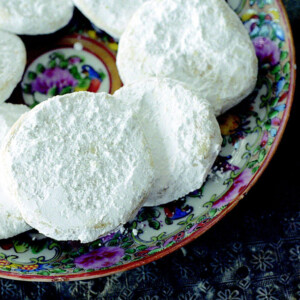 Lemon meltaway cookies, covered in icing sugar, piled on a deep blue patterned plate.