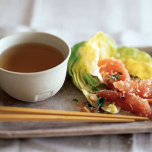 Pomelo salad piled on a rectangular ceramic plate, with chopsticks and a bowl of dressing.