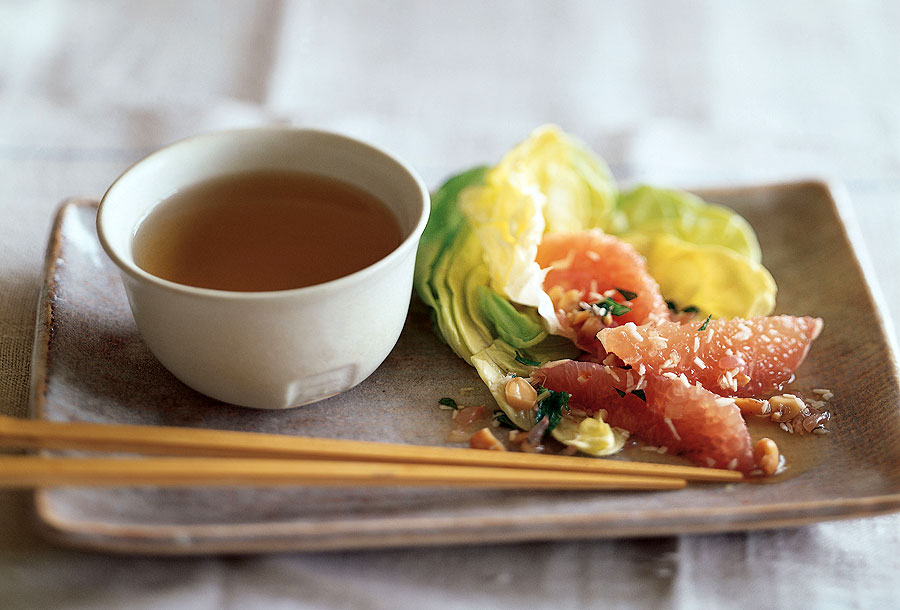 Pomelo salad piled on a rectangular ceramic plate, with chopsticks and a bowl of dressing.