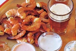 Shrimp with three dipping sauces piled on a platter, beside a glass of ale