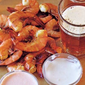 Shrimp with three dipping sauces piled on a platter, beside a glass of ale