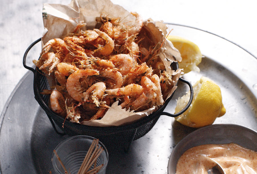 A basket of spiced shrimp with a bowl of paprika mayonnaise beside the shrimp, a halved lemon, and a cup of toothpicks.