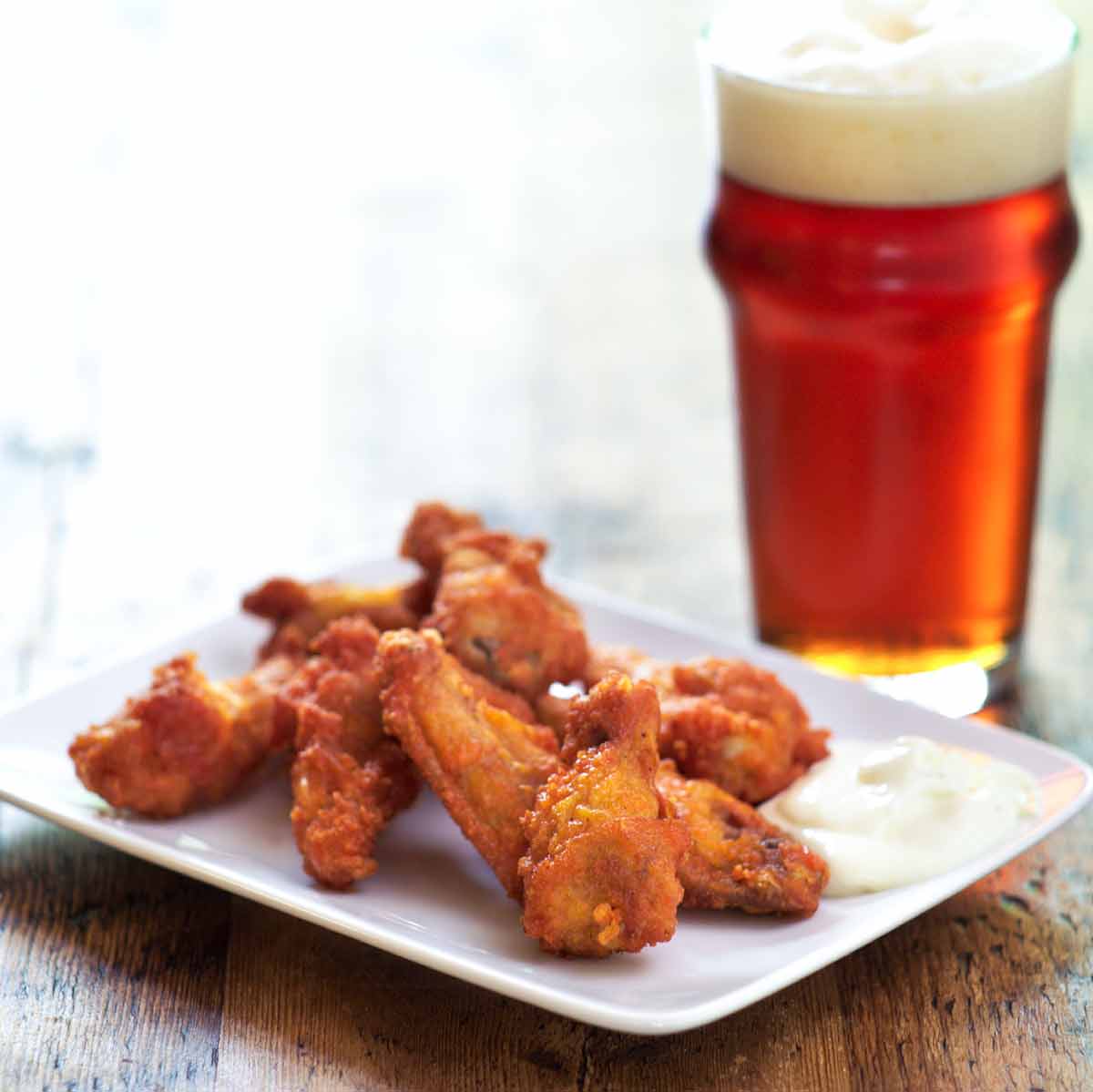 A pile of Tabasco chicken wings on a white plate with some ranch dip.