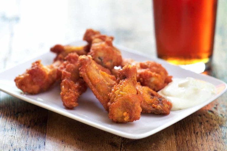 A pile of Tabasco chicken wings on a white plate with some ranch dip.