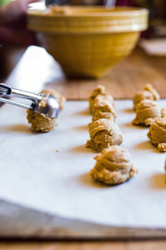 Rows of peanut butter sandies dough balls with a cookie scoop placing another dough ball on the surface.