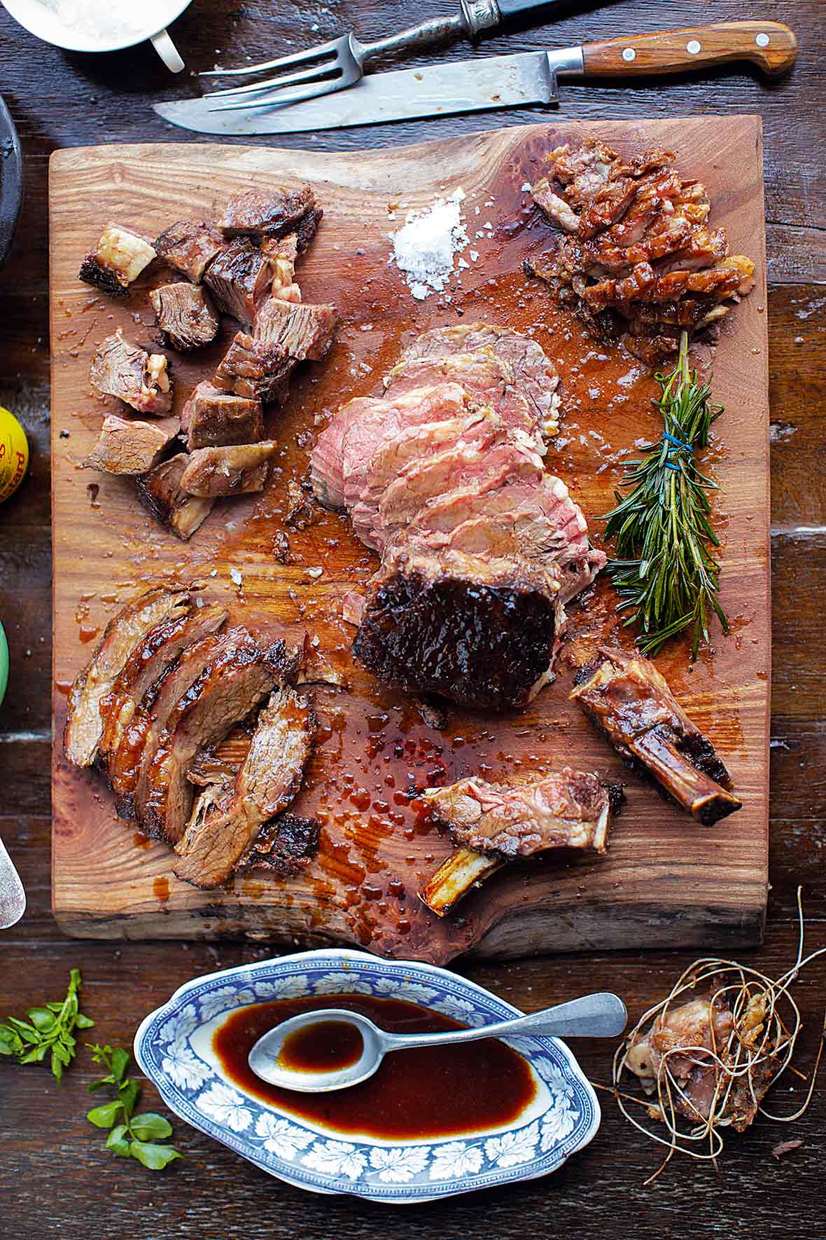 Slices of medium rare roast beef meat on wooden cutting board, pepper and  rosemary branches on wooden background. Top view. Gourmet food. Raw meat  beef steak. Stock Photo