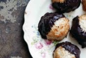 Five coconut macaroons dipped in chocolate arranged on a floral-patterned china plate.