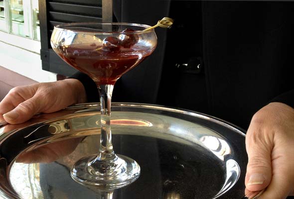 A Fatty Daddy cocktail in a coupe glass on a silver tray, being held by a man.