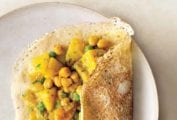 A rava dosa filled with potato and chickpea masala partially folded over on a white ceramic plate.