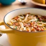 A yellow Dutch oven filled with white bean and chicken chili, topped with pieces of bacon.